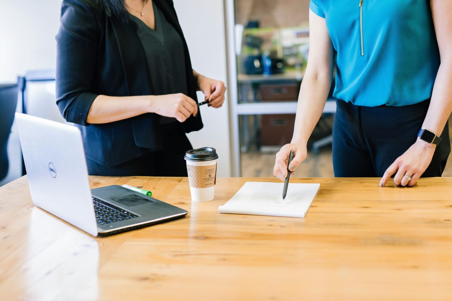 Two business colleagues reviewing notes together at a table, one pointing out a detail to the other