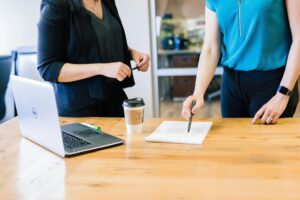 Two business colleagues reviewing notes together at a table, one pointing out a detail to the other